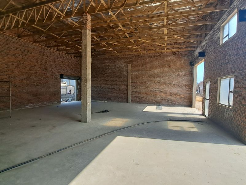 Spacious industrial open-plan warehouse area featuring exposed brick walls, timber roof trusses, and concrete flooring, currently in an unfinished state.