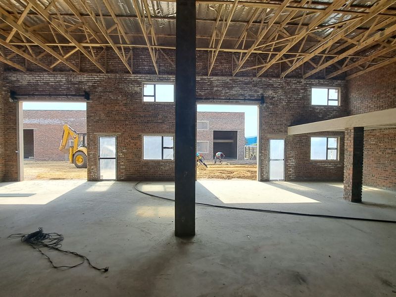 Spacious industrial open-plan area under construction, featuring exposed brick walls, timber roof trusses, and a mezzanine level with large openings to the exterior.