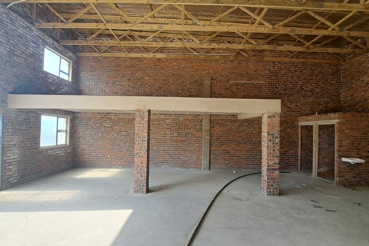 Spacious industrial open-plan area featuring exposed brick walls, timber roof trusses, and a concrete mezzanine level, currently in an unfinished construction state.