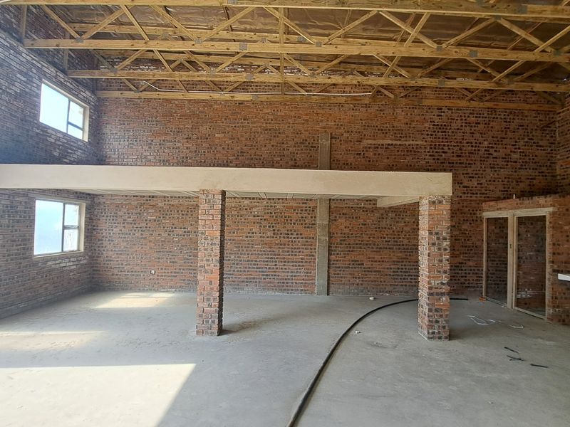 Spacious industrial open-plan area featuring exposed brick walls, timber roof trusses, and a concrete mezzanine level, currently in an unfinished construction state.