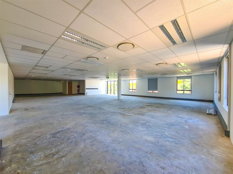 A large, open-plan office space featuring a suspended ceiling with recessed lighting and expansive windows, currently in a shell condition awaiting flooring finishes.