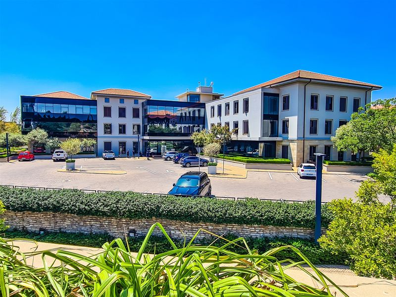 A professional multi-story office building featuring a paved parking lot, well-maintained landscaping, and a modern facade with large glass windows.