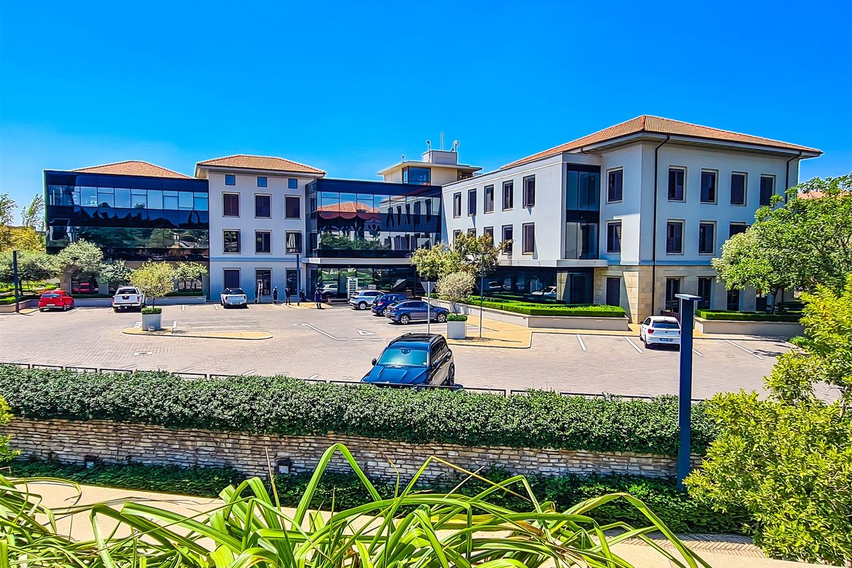 A professional multi-story office building featuring a paved parking lot, well-maintained landscaping, and a modern facade with large glass windows.