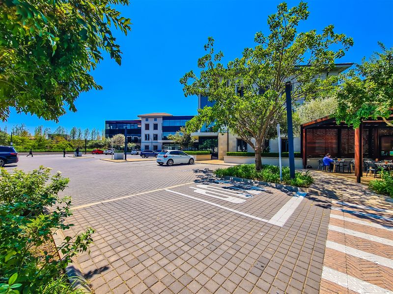 A well-maintained commercial office exterior featuring a paved parking area, landscaped greenery, and a covered outdoor seating space.
