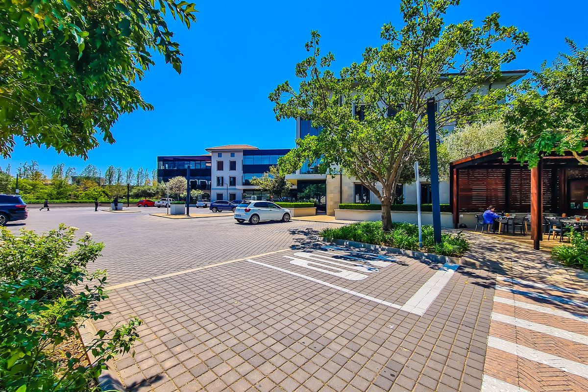 A well-maintained commercial office exterior featuring a paved parking area, landscaped greenery, and a covered outdoor seating space.