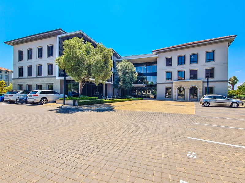 Modern multi-story office building featuring a paved parking forecourt, glass facade elements, and well-maintained stone and render exterior finishes.