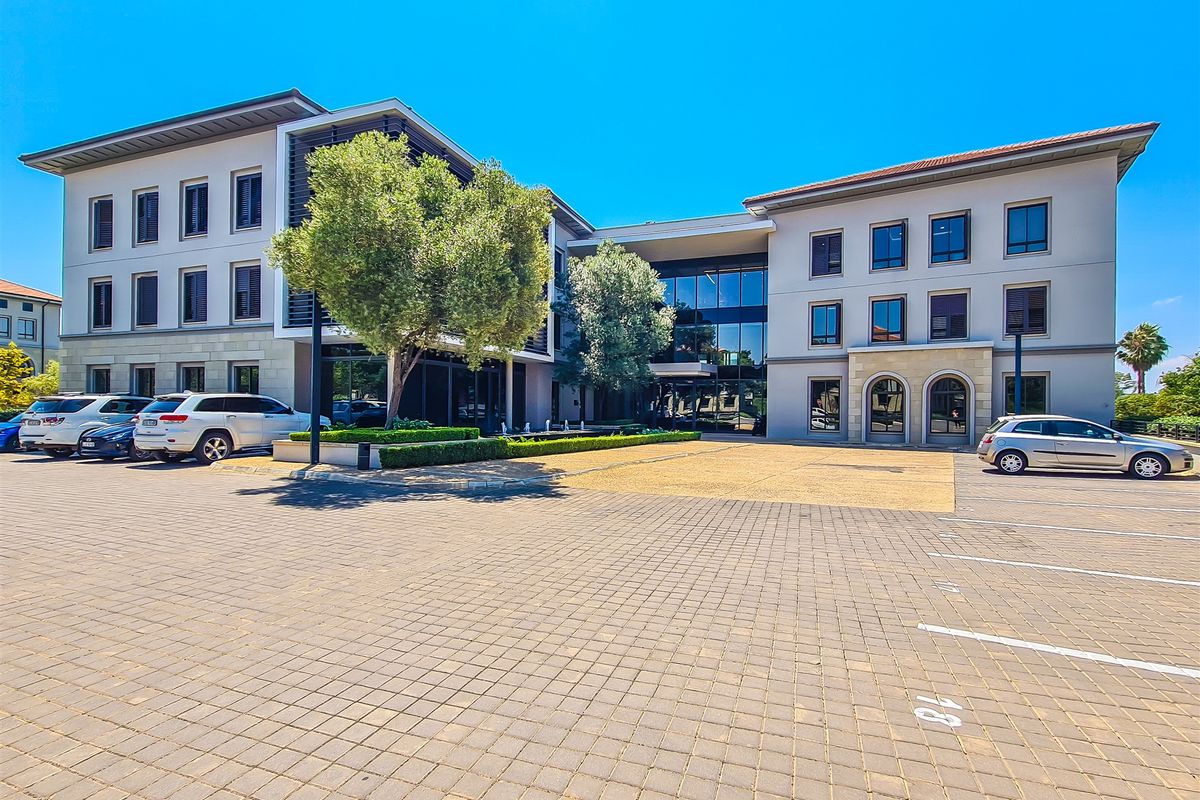 Modern multi-story office building featuring a paved parking forecourt, glass facade elements, and well-maintained stone and render exterior finishes.