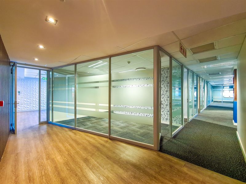 Modern office space featuring glass-partitioned meeting rooms, recessed lighting, and a combination of carpet and laminate flooring in a professional commercial setting.