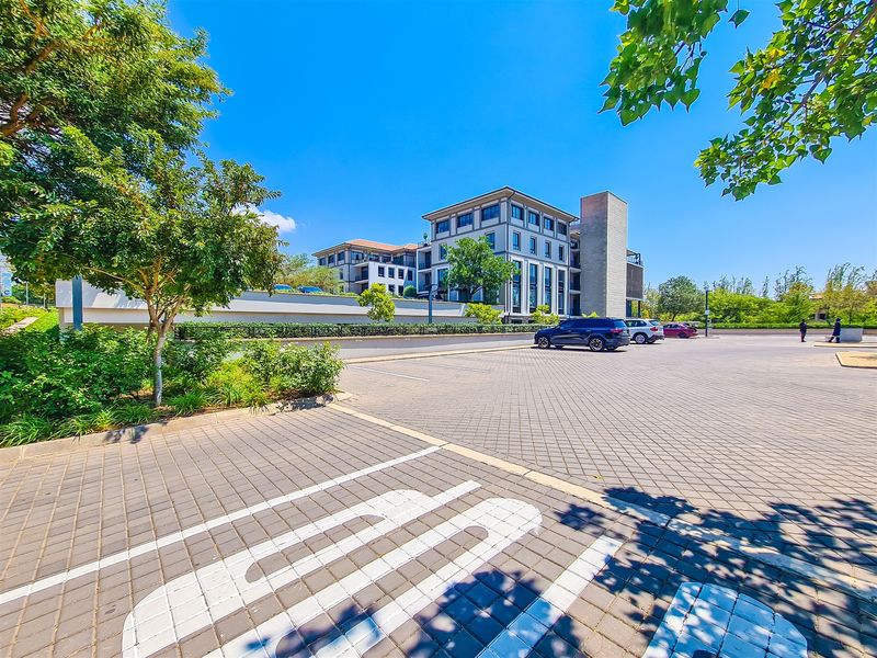 A well-maintained multi-story office building featuring a paved parking area and landscaped surroundings under a clear blue sky.