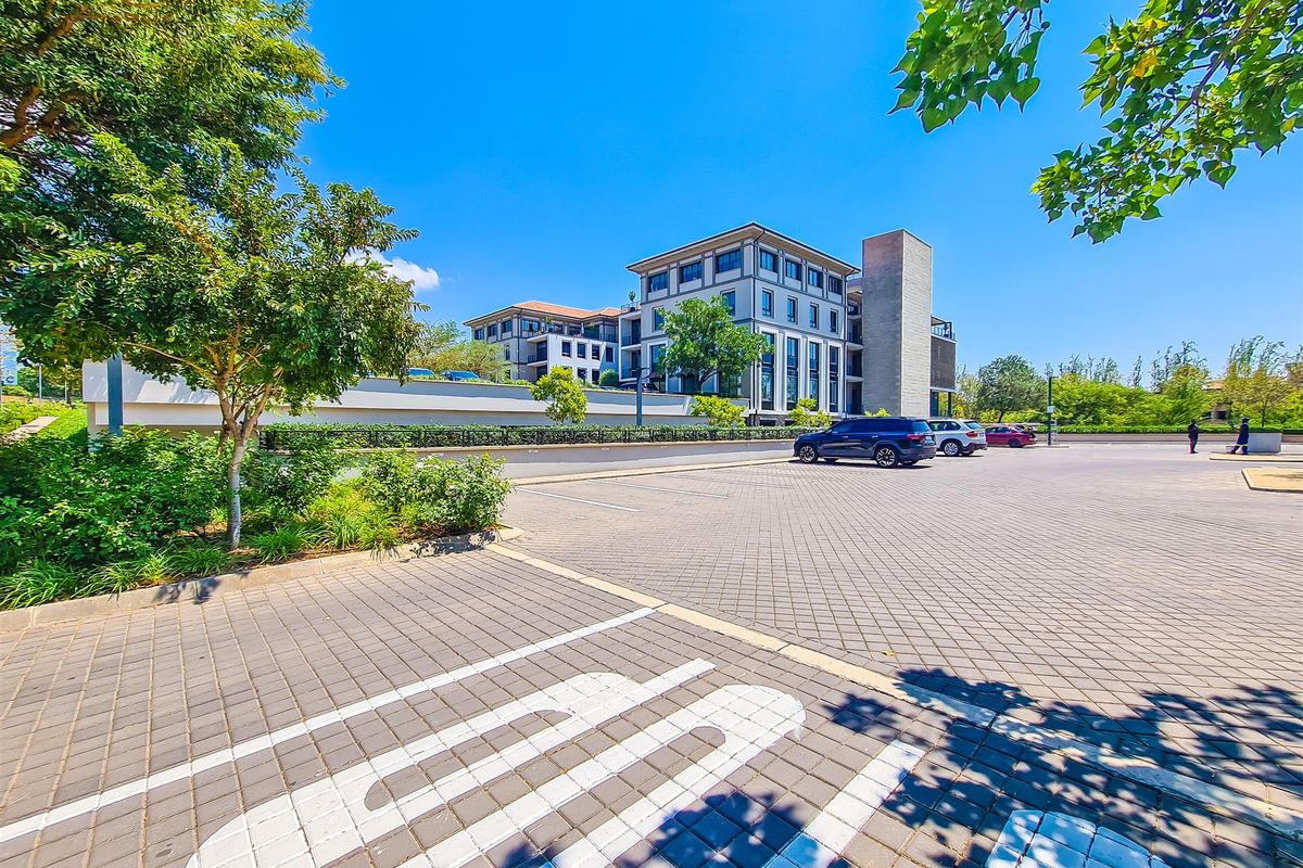 A well-maintained multi-story office building featuring a paved parking area and landscaped surroundings under a clear blue sky.
