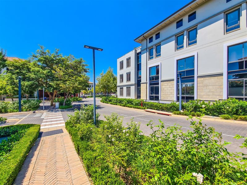 A well-maintained exterior view of a modern office building featuring paved access, landscaped greenery, and large glass windows under a clear sky.