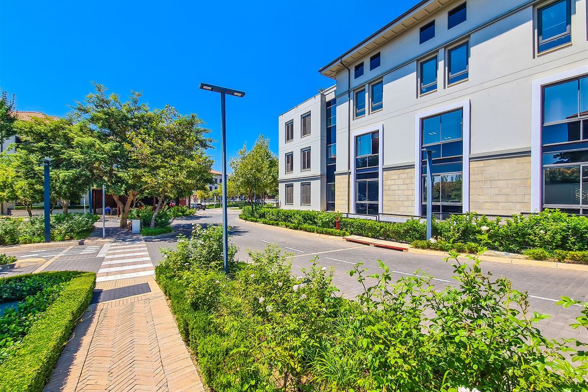 A well-maintained exterior view of a modern office building featuring paved access, landscaped greenery, and large glass windows under a clear sky.