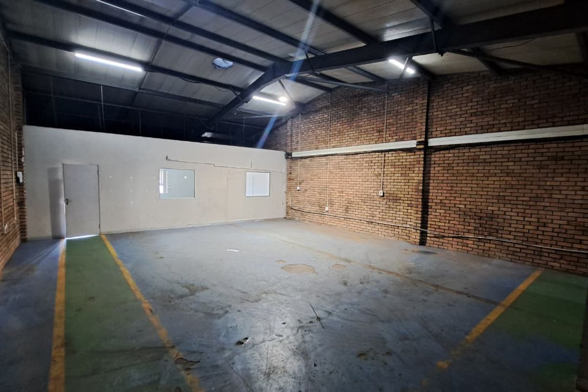 Spacious industrial utility area featuring exposed brick walls, steel roof trusses, and durable painted concrete flooring, suitable for storage or workshop use.