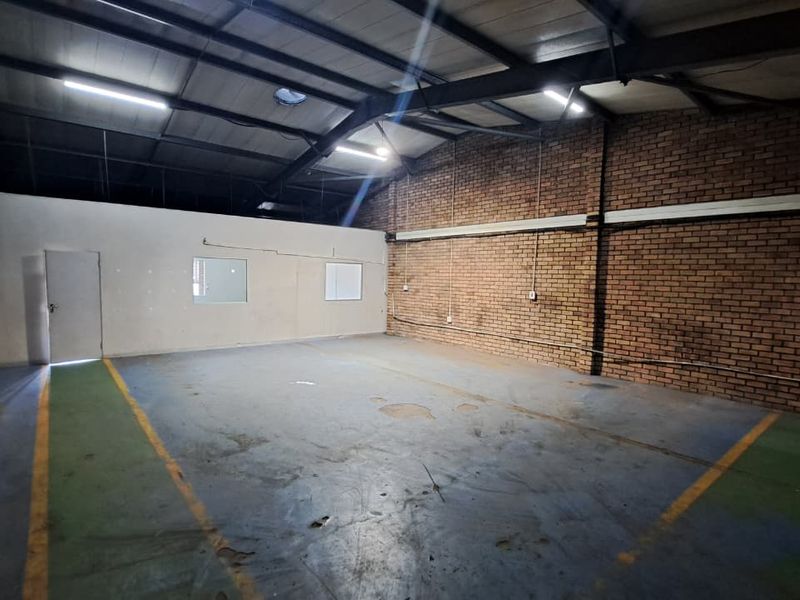 Spacious industrial utility area featuring exposed brick walls, steel roof trusses, and durable painted concrete flooring, suitable for storage or workshop use.