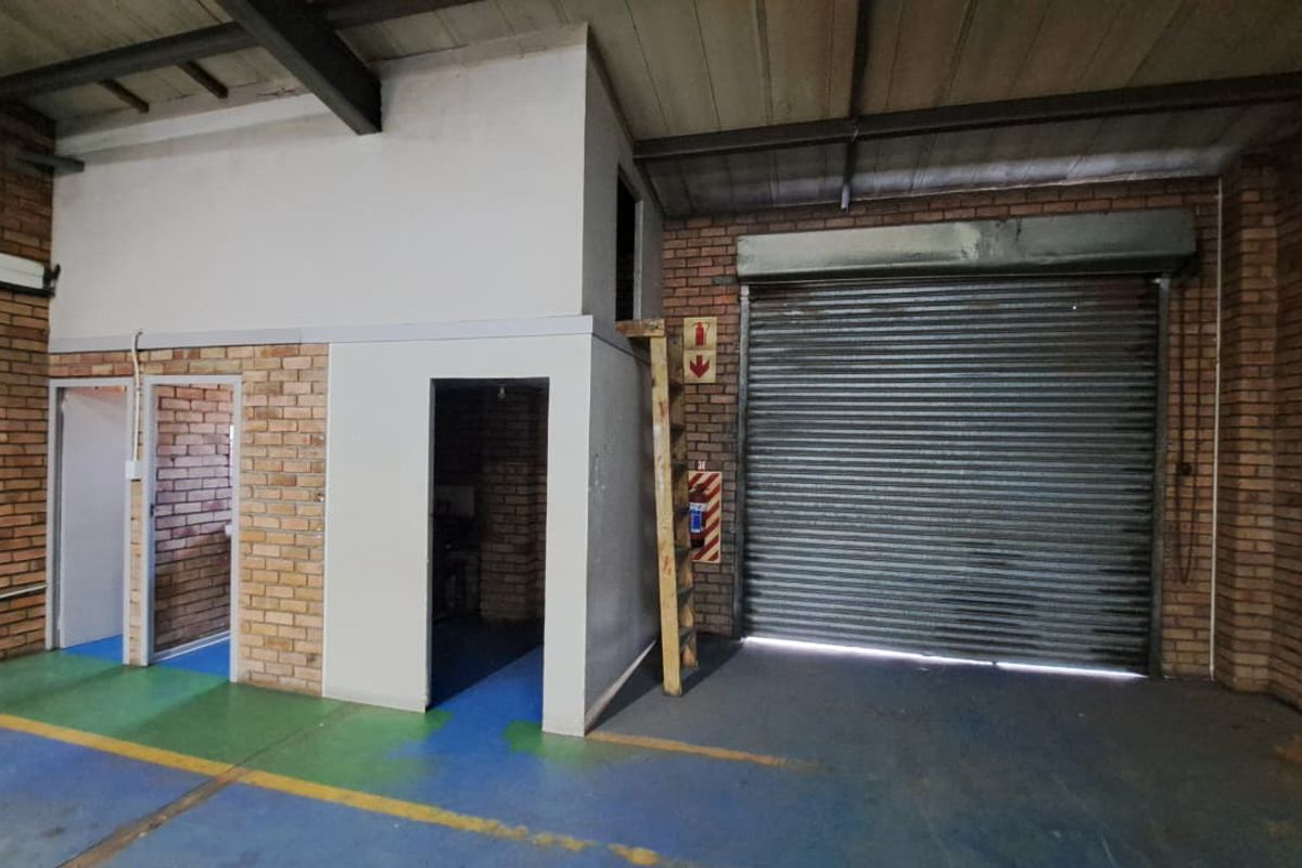 Industrial utility space featuring exposed brickwork, high ceilings with steel trusses, a large roller shutter door, and a mezzanine access ladder.