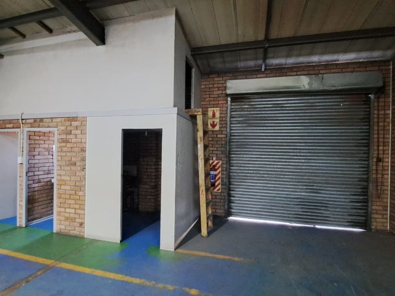 Industrial utility space featuring exposed brickwork, high ceilings with steel trusses, a large roller shutter door, and a mezzanine access ladder.