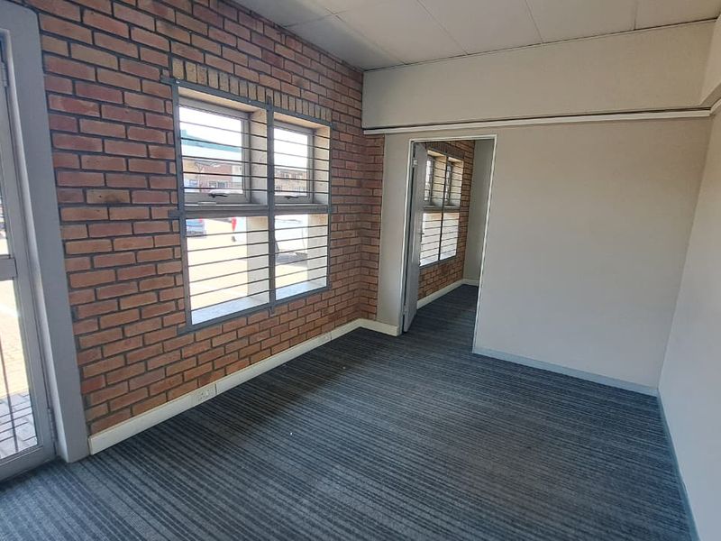 An empty office space featuring exposed brick walls, carpeted flooring, and security bars on the windows, providing a functional industrial workspace.