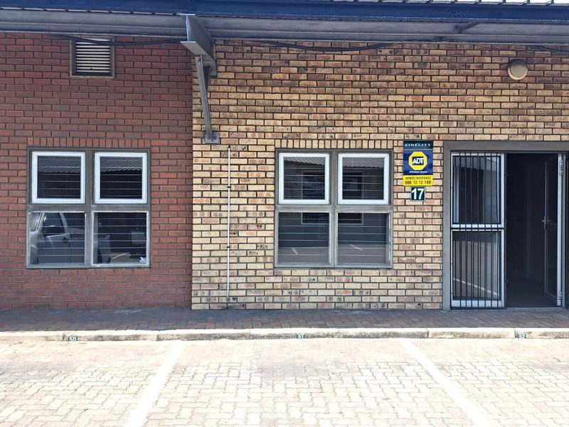 Front exterior view of an industrial unit featuring face brick facade, paved parking bays, and secure access points with security gates.