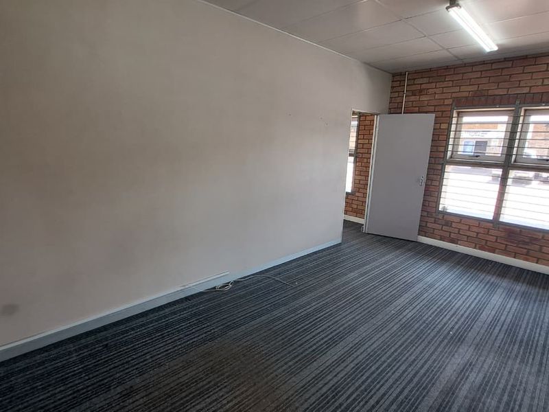 An empty office space featuring exposed brickwork, fluorescent lighting, and carpeted flooring, suitable for a functional industrial workspace.
