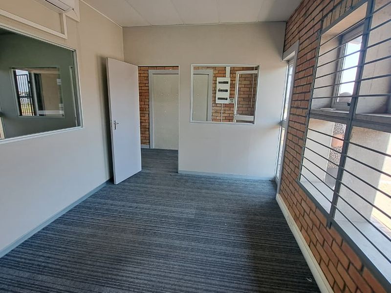 A clean, empty office space featuring exposed brick walls, carpeted flooring, security bars on windows, and internal glass partitions for a professional industrial aesthetic.