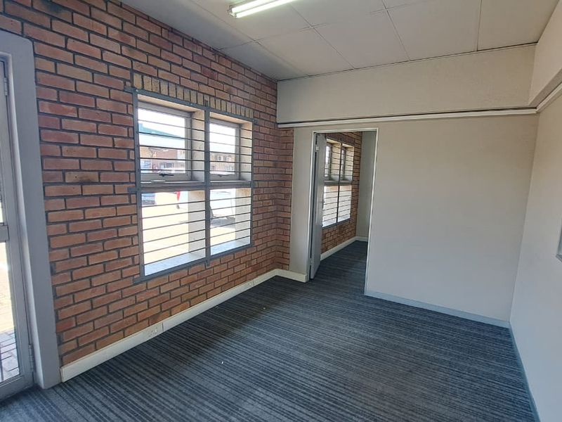 An empty office space featuring exposed brickwork, security-barred windows, carpeted flooring, and a drop ceiling, suitable for professional use.