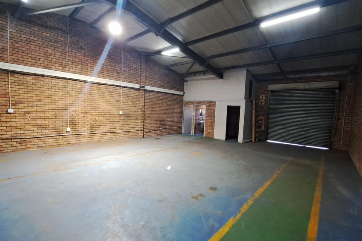 Spacious industrial warehouse unit featuring exposed brick walls, concrete flooring, high ceilings with steel trusses, and a large roller shutter door for easy access.