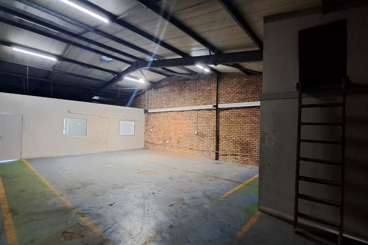 Spacious industrial utility area featuring exposed brickwork, steel roof trusses, concrete flooring, and a fixed access ladder to an upper level.