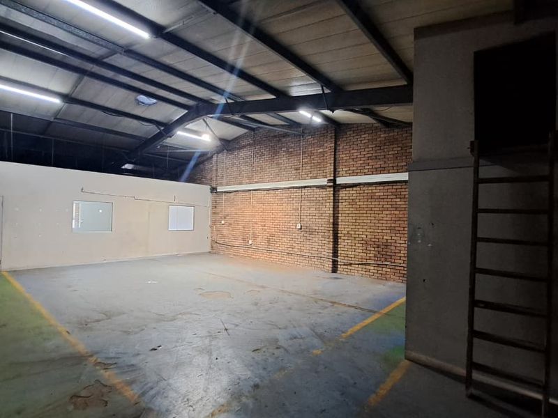 Spacious industrial utility area featuring exposed brickwork, steel roof trusses, concrete flooring, and a fixed access ladder to an upper level.