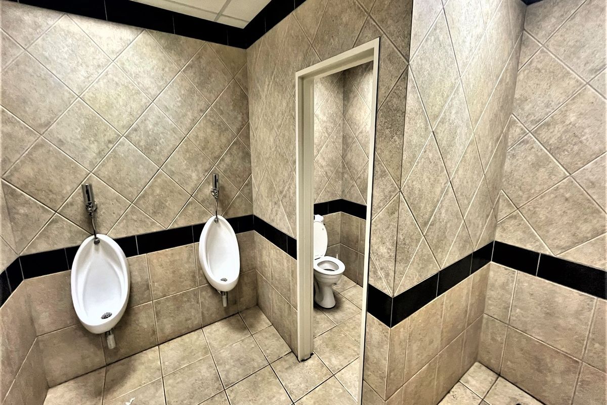 A commercial restroom facility featuring wall-mounted urinals and a separate toilet cubicle with tiled walls and flooring.