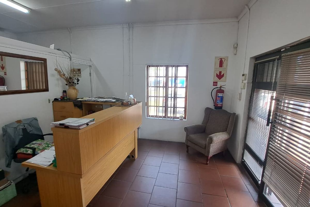 A functional office reception area featuring tiled flooring, a built-in reception desk, security window bars, and an aluminium-framed glass entrance door.