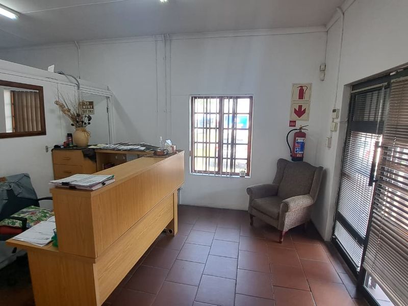 A functional office reception area featuring tiled flooring, a built-in reception desk, security window bars, and an aluminium-framed glass entrance door.
