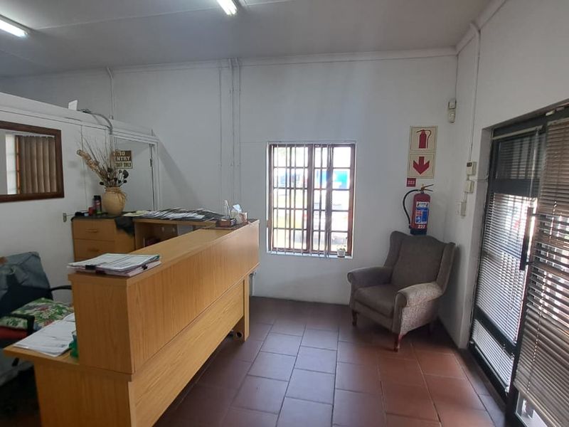 A functional office reception area featuring tiled flooring, security window bars, and a built-in reception counter, suitable for professional business operations.