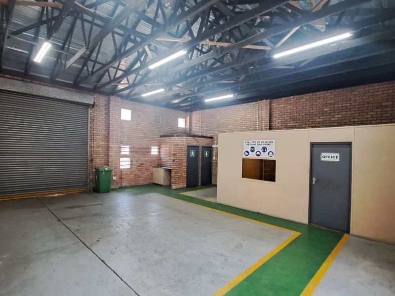 Spacious industrial utility area featuring exposed brick walls, high steel roof trusses, a large roller shutter door, and a dedicated internal office partition.