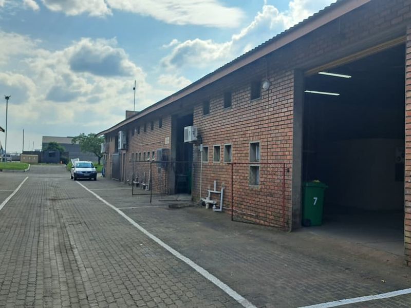 Exterior view of an industrial warehouse complex featuring face brick construction, paved driveway access, and multiple roller shutter door entry points.