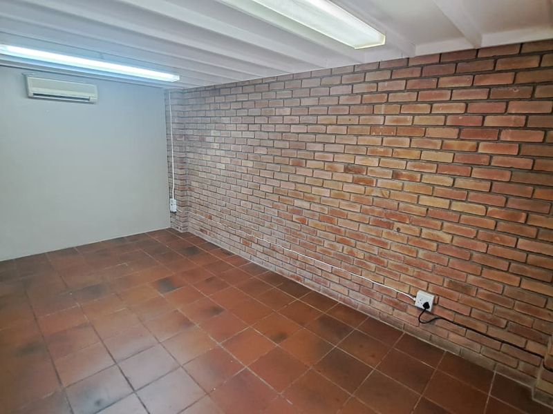 An empty office space featuring exposed brick walls, tiled flooring, and a wall-mounted air conditioning unit, providing a functional industrial-style workspace.