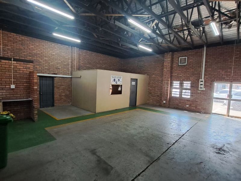 Spacious industrial utility area featuring exposed brick walls, high ceilings with steel trusses, concrete flooring, and a built-in office partition.