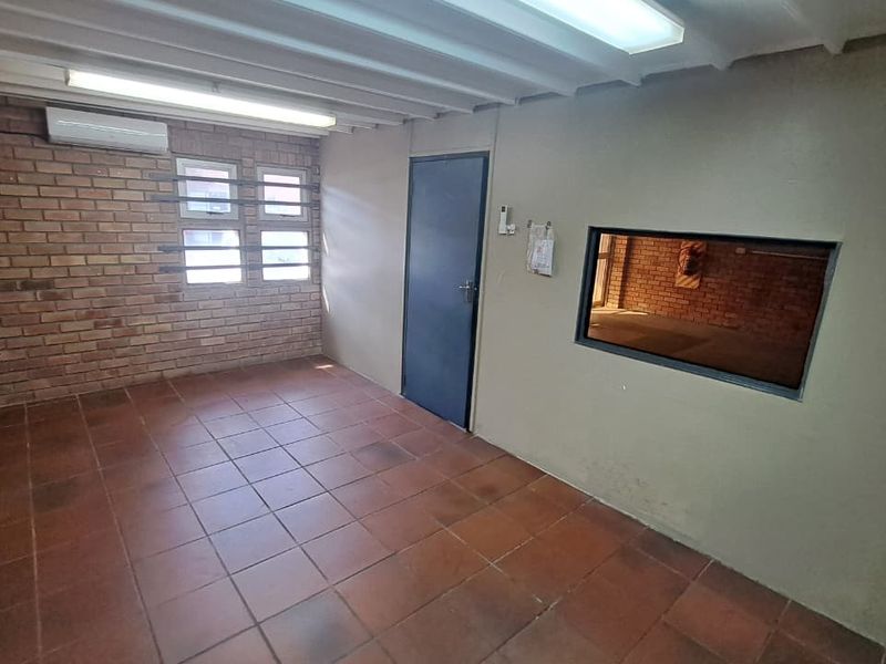 A functional industrial office space featuring exposed brick walls, tiled flooring, an integrated air conditioning unit, and an internal viewing window.