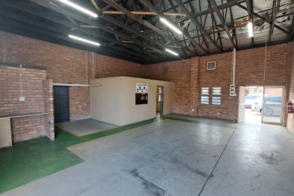 Spacious industrial utility area featuring exposed brick walls, high ceilings with exposed trusses, concrete flooring, and a partitioned office space.