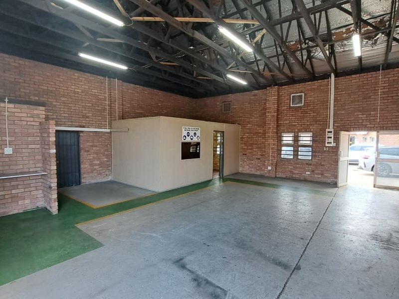 Spacious industrial utility area featuring exposed brick walls, high ceilings with exposed trusses, concrete flooring, and a partitioned office space.