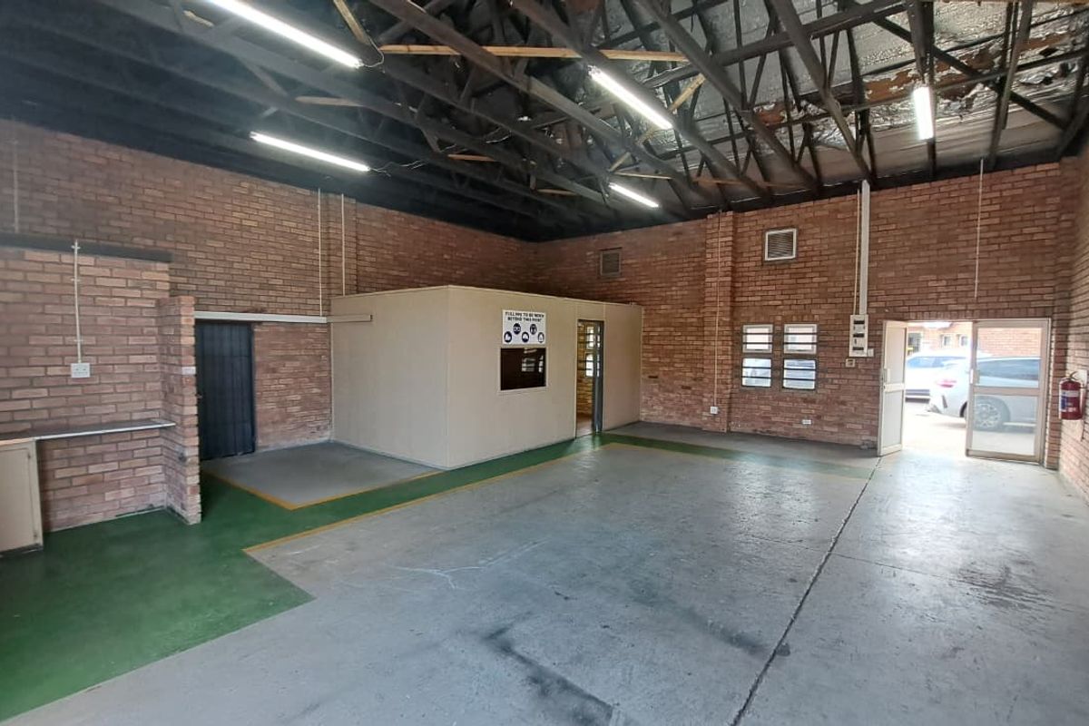 Spacious industrial utility area featuring exposed brick walls, high steel truss ceilings, concrete flooring, and a partitioned office space with secure access.