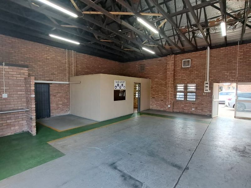 Spacious industrial utility area featuring exposed brick walls, high steel truss ceilings, concrete flooring, and a partitioned office space with secure access.
