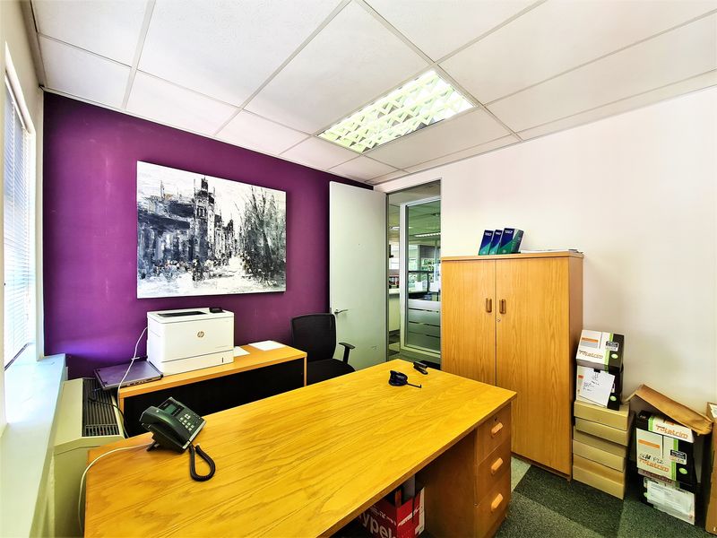 A functional office space featuring a suspended ceiling with recessed lighting, carpeted flooring, and a glass-paneled door leading to an adjacent area.