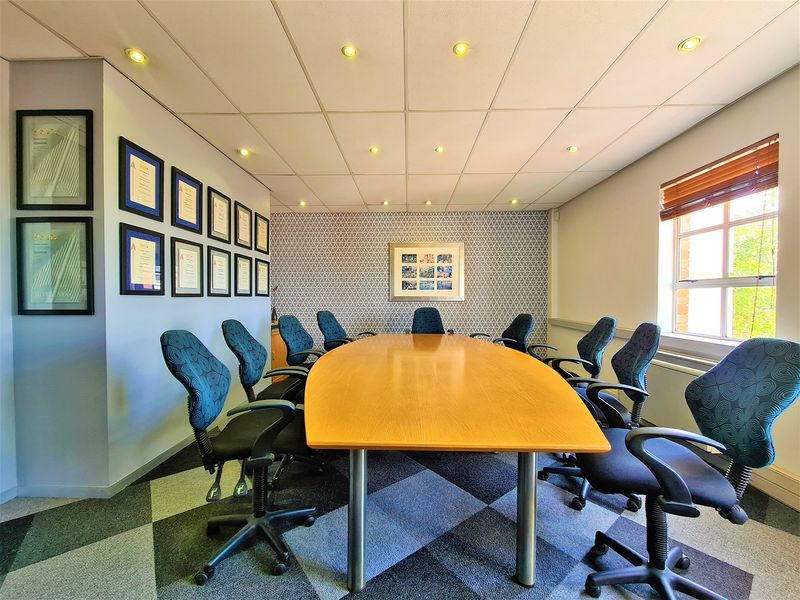 A professional boardroom featuring a suspended ceiling with recessed lighting, patterned accent wallpaper, and durable carpet tiles.