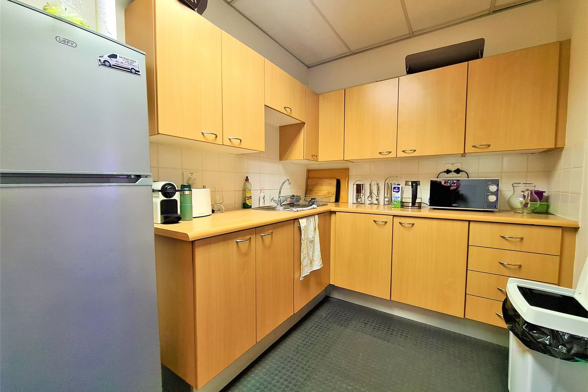 A functional office kitchenette featuring light wood-finish cabinetry, laminate countertops, a stainless steel sink, and a tiled backsplash.