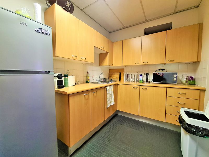 A functional office kitchenette featuring light wood-finish cabinetry, laminate countertops, a stainless steel sink, and a tiled backsplash.