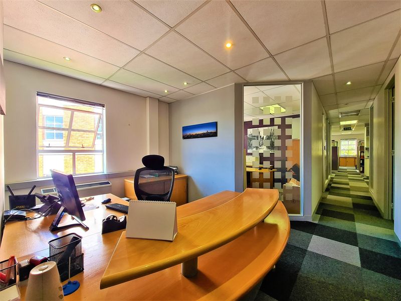 A professional office space featuring a built-in desk, glass partition wall, suspended ceiling with recessed lighting, and patterned carpet tiles.