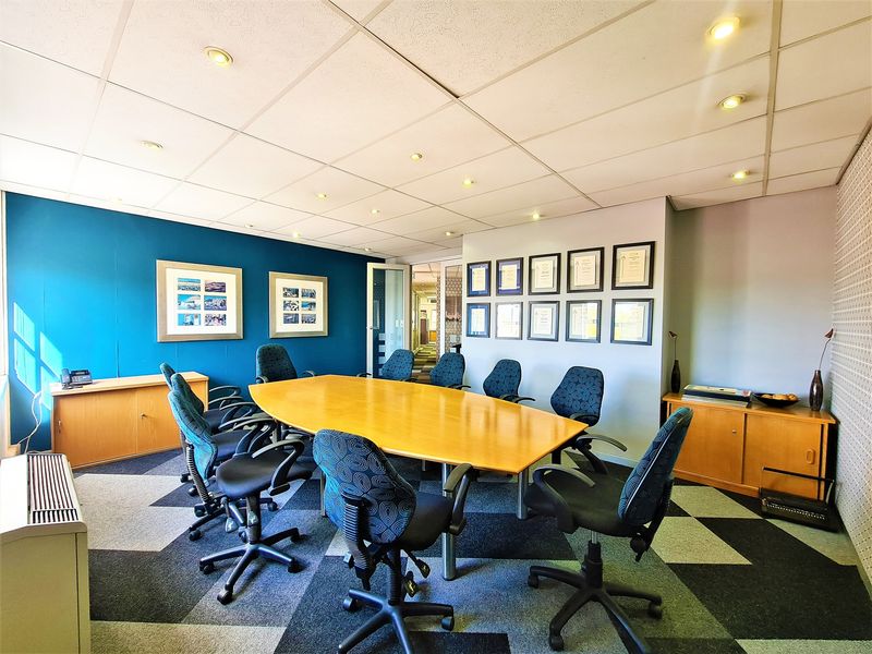 A professional office boardroom featuring a suspended ceiling with recessed lighting, carpet tiles, and built-in storage cabinetry.
