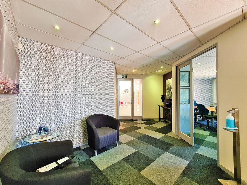 A professional office reception area featuring patterned wallpaper, carpet tiles, and a glass partition door leading into a connected workspace.