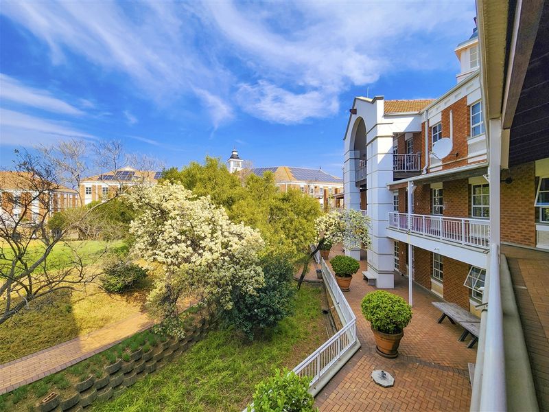 A view of the office building's rear exterior, featuring a multi-level brick facade, balconies, and a landscaped garden area with paved walkways.