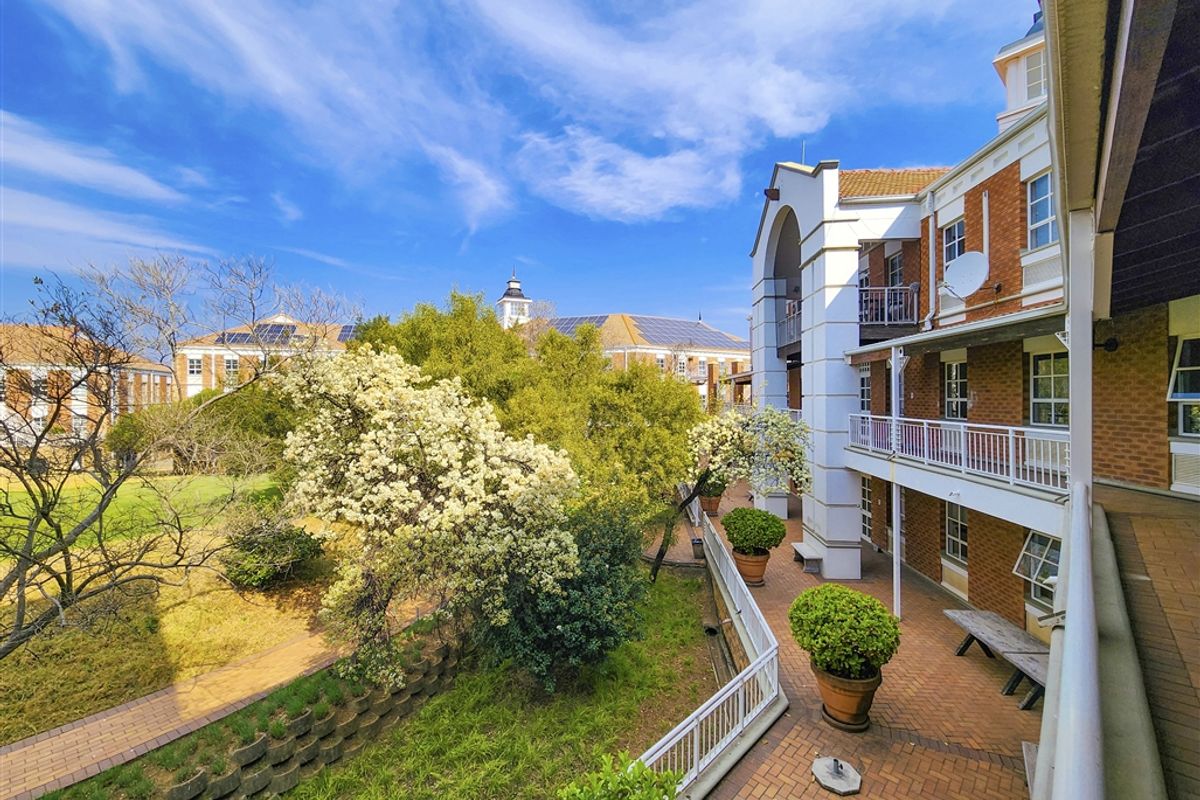 A view of the office building's rear exterior, featuring a multi-level brick facade, balconies, and a landscaped garden area with paved walkways.